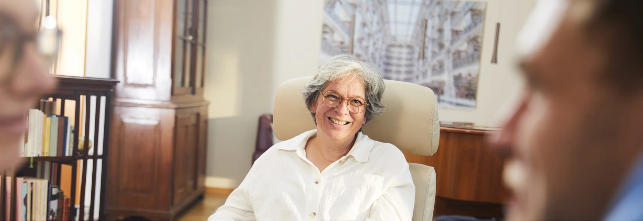 Dorothee Bremer smiling in her armchair during a session, seen past the shoulders of the two people opposite her